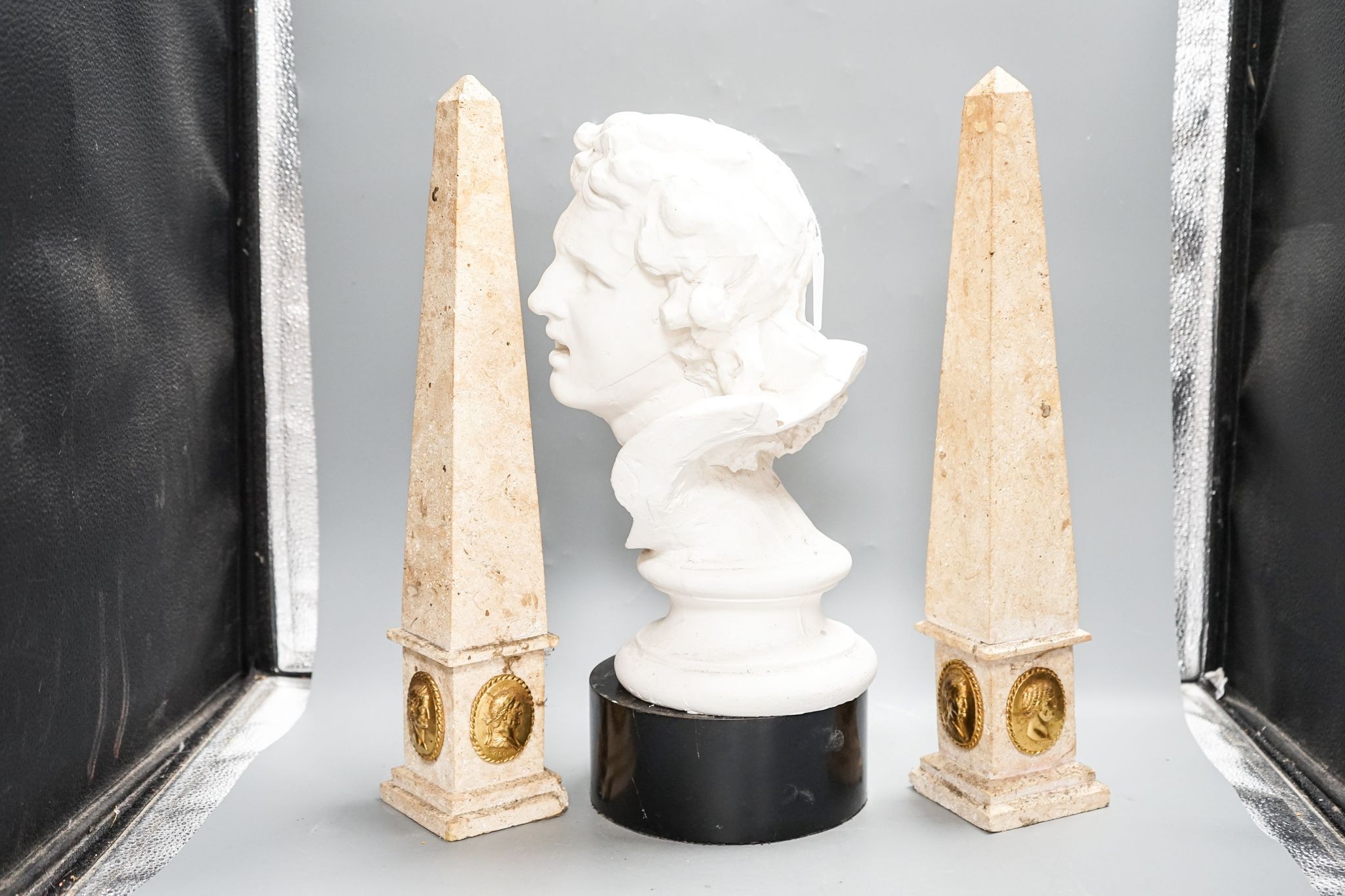 A pair of composition classical faux marble obelisks together with a pair of simulated stone Sphinx, a faux bronze model of Trajan‘s column and a faux marble bust (5)